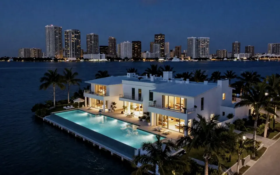 Waterfront home with a lit pool at night, city towers across the bay